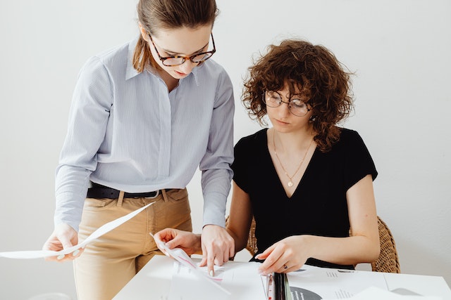 Two people wearing glasses looking at a sheet of paper together